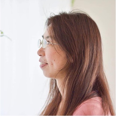 赤褐色のタートルネックと白いバッグを身に付けた女性の横顔。目を閉じて見上げている。